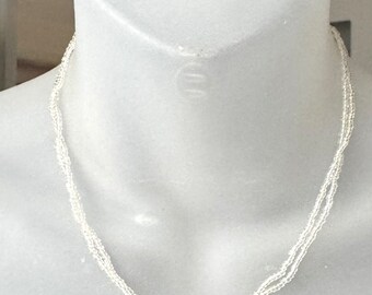 May include: A delicate, multi-strand necklace made of tiny, clear beads. The necklace is layered and hangs close to the neck.