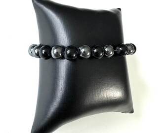 Op de afbeelding: Een elastische armband met afwisselend ronde kralen in glanzend zwart en metallic donkergrijs. De kralen zijn in een herhalend patroon geregen, wat zorgt voor een glad, reflecterend oppervlak dat het licht over de hele band opvangt.