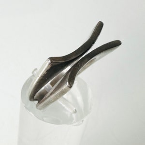May include: A silver ring with a unique, abstract design. The ring is made of two pieces of metal that are joined together in a way that creates a V-shape.