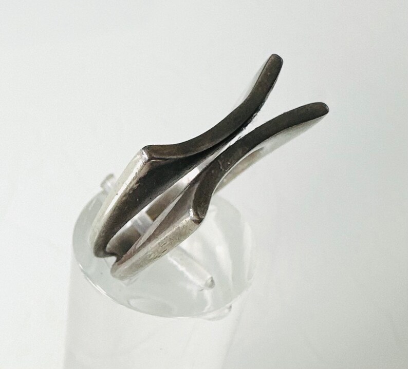 May include: A silver ring with a unique, abstract design. The ring is made of two pieces of metal that are joined together in a way that creates a V-shape.