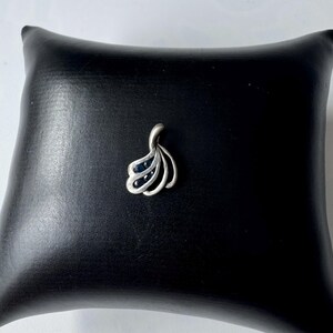 Op de afbeelding: Een zilveren hanger met een waaiervormig ontwerp met zwarte edelstenen.