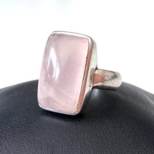 Könnte beinhalten: Ein Silberring mit einem großen, rechteckigen Rosenquarzstein. Der Stein hat eine zarte rosa Farbe und eine polierte Oberfläche. Der Ring hat ein schlichtes, modernes Design.