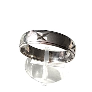 Könnte beinhalten: Ein silberfarbener Ring mit geprägten sternförmigen Mustern. Der Ring wird auf einem transparenten Ständer vor weißem Hintergrund präsentiert. Das Band des Rings ist etwa 0,64 cm breit.