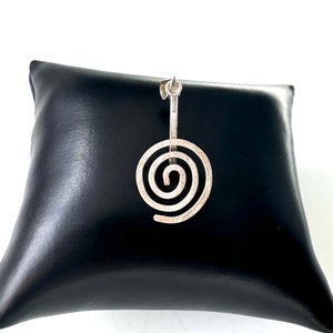 May include: Silver pendant featuring a spiral design. The pendant is on a black display stand.