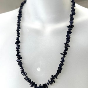 Peut inclure: Un collier bleu foncé composé de pierres polies de forme irrégulière. Les pierres sont enfilées pour former un long collier. Le collier est présenté sur un mannequin blanc. Les pierres ont un léger éclat.