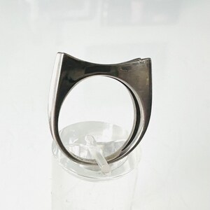 May include: A silver ring with a unique, angular design. The ring is made of a smooth, polished metal and has a simple, modern aesthetic.