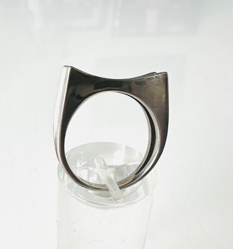 May include: A silver ring with a unique, angular design. The ring is made of a smooth, polished metal and has a simple, modern aesthetic.