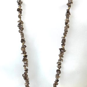 May include: A long necklace featuring numerous small, irregular, translucent brown smoky quartz chip beads strung together with tiny, round, metallic gold-toned spacer beads interspersed throughout the length of the strand.