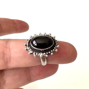 May include: A silver ring with a black oval gemstone set in a circular, beaded design.