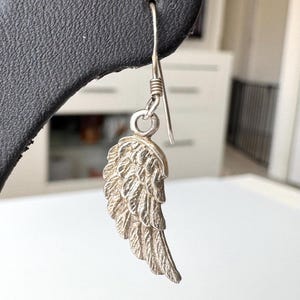 Pu&ograve; includere: Un singolo orecchino color argento a forma di ala dettagliata. L'orecchino &egrave; appeso a un semplice gancio e presenta intricati dettagli di piume. L'ala &egrave; leggermente curva, conferendole un aspetto realistico. L'orecchino &egrave; esposto su uno sfondo nero.