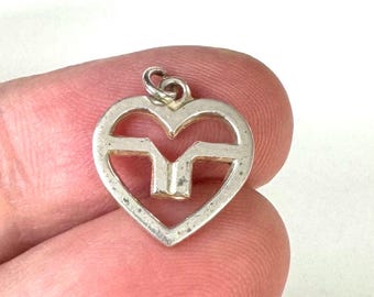 May include: A silver charm in the shape of a heart with a stylised letter M inside.