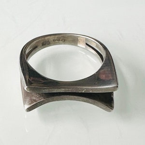 May include: A silver ring with a geometric design. The ring is marked "925" on the inside band.