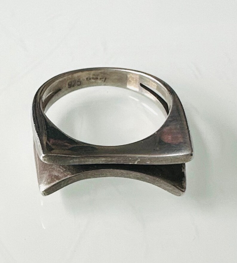 May include: A silver ring with a geometric design. The ring is marked "925" on the inside band.