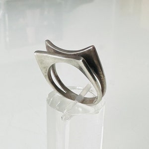 May include: A silver ring with a geometric design. The ring is made of two pieces of metal that are joined together to form a unique shape.