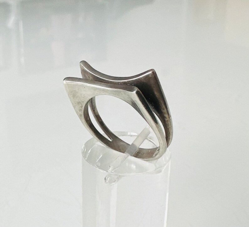 May include: A silver ring with a geometric design. The ring is made of two pieces of metal that are joined together to form a unique shape.