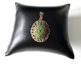 May include: A gold-toned pendant with an oval-shaped green, blue, and pink enamel design. The pendant has a delicate filigree border.