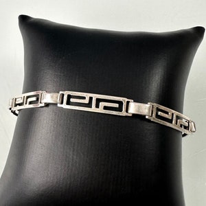 May include: A silver bracelet featuring a geometric pattern. The bracelet is made of interlocking links that create a repeating design.