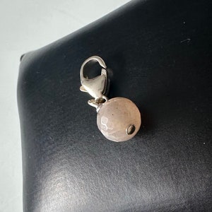 Peut inclure: Un charme argenté avec une perle ronde texturée rose clair attachée à un fermoir argenté.