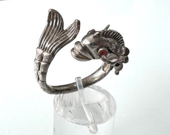 May include: Silver fish ring with a red stone eye. The fish is curled into a circle with its tail wrapping around the ring.