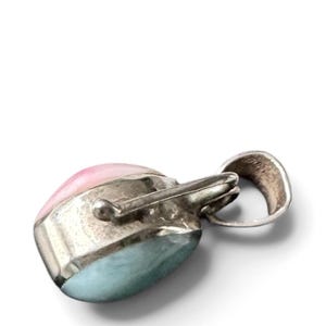 May include: A pendant featuring a smooth, rounded stone with a dual-tone appearance, displaying a soft pink section transitioning into a pale blue base. The stone is encased in a polished silver setting with a prominent, curved bail for attachment.