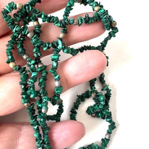 May include: A necklace composed of small, irregularly shaped, deep green malachite stones interspersed with silver-toned beads. The necklace is displayed against a white background.