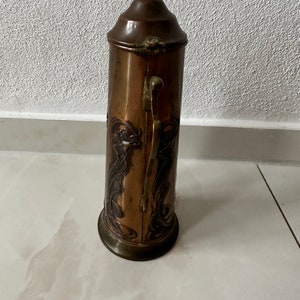 May include: A copper and brass vintage boot scraper with an ornate Art Nouveau design. The scraper has a hinged lid and a handle on the side.