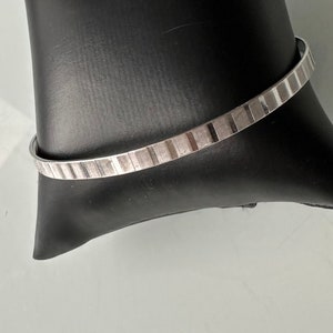 Peut inclure: Un bracelet jonc argenté avec un motif texturé rayé.