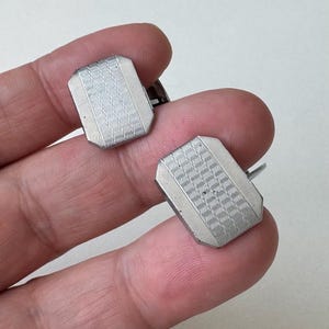 May include: A pair of silver-toned cufflinks. Each cufflink has a rectangular shape with a detailed, wavy pattern in the center. The cufflinks are shown against a neutral background.
