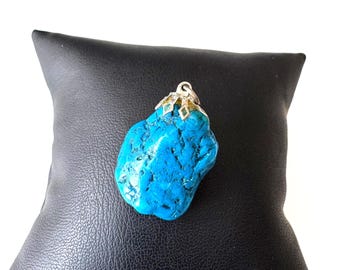 May include: A raw, bright blue turquoise pendant with a textured, irregular surface. The stone is secured by a silver-toned metal cap featuring a small, integrated loop at the top for attachment to a chain or cord, showcasing a natural aesthetic.