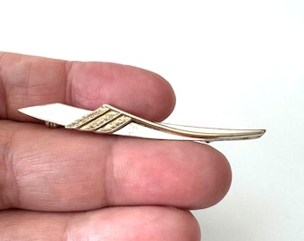 May include: A slender, elongated brooch featuring a polished silver-tone finish with a contrasting gold-tone textured section near the center. The design is tapered at both ends, creating a sleek, curved shape that spans the width of the fingers.