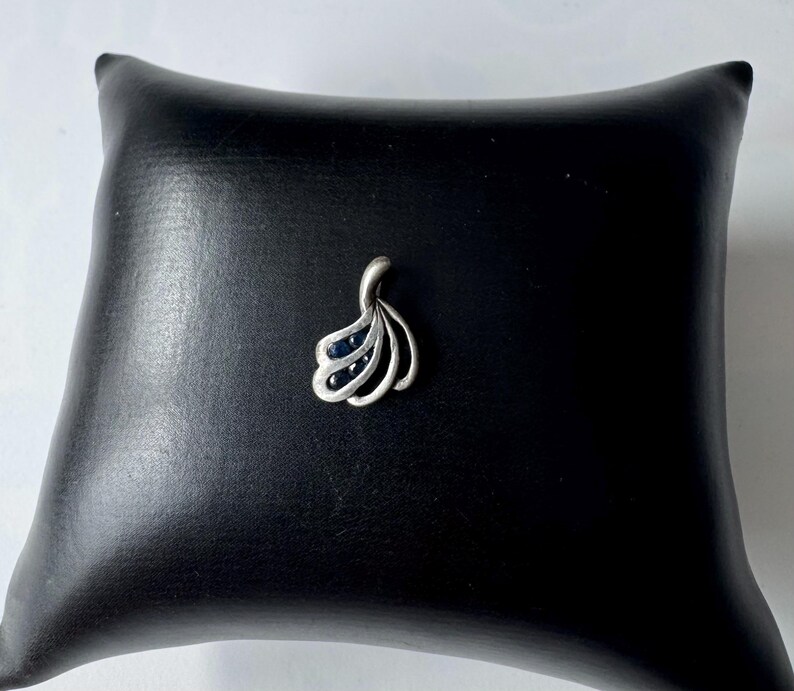 Op de afbeelding: Een zilveren hanger met een waaiervormig ontwerp met zwarte edelstenen.