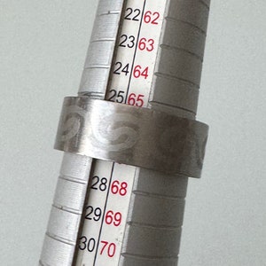 Op de afbeelding: Een zilveren ring met een getextureerd ontwerp wordt getoond op een ringmaat. De ringmaat toont maten 22 tot 30.