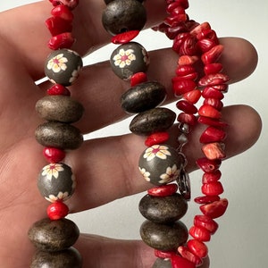 May include: A multi-strand necklace with red coral beads and gray wooden beads with white flower designs.