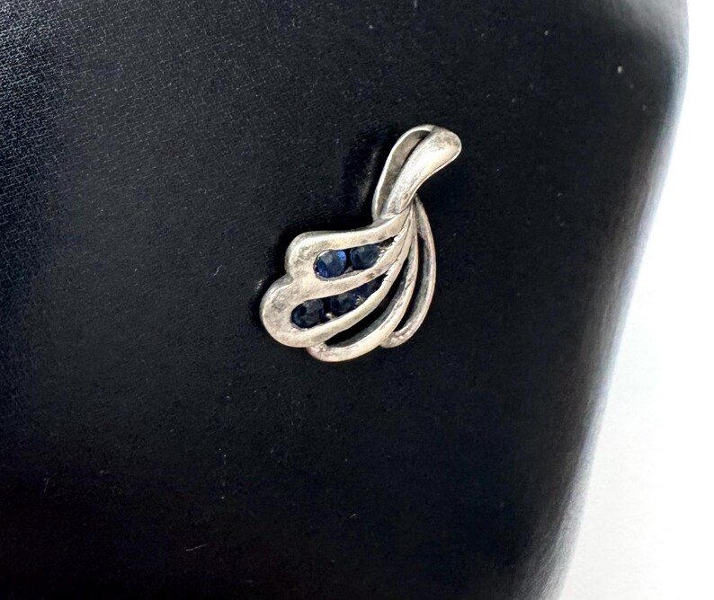 Op de afbeelding: Een zilveren hanger in de vorm van een blad met blauwe edelstenen in het midden.