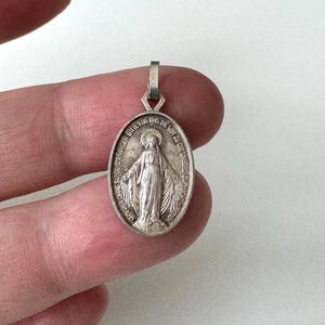 May include: Silver oval pendant featuring a depiction of the Virgin Mary with the text "OHNE SUNDE ERFANGEN BITTE FUR UNS DIE WIR ZU DIR UNSERE ZUFLICHT MRHYENT" around the border.
