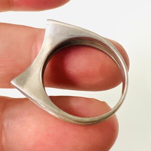 May include: A silver ring with a unique, angular design. The ring is made of a single piece of metal and has a smooth, polished finish.