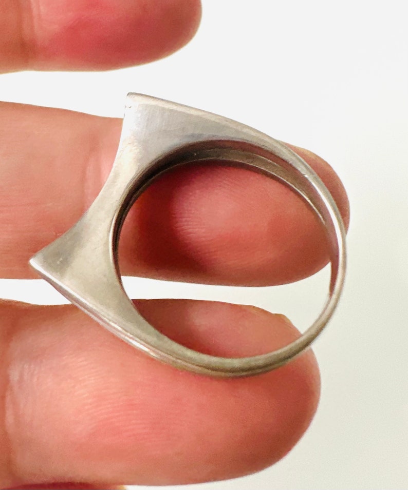 May include: A silver ring with a unique, angular design. The ring is made of a single piece of metal and has a smooth, polished finish.