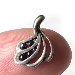 Op de afbeelding: Een zilveren hanger met een delicaat, abstract ontwerp met meerdere gebogen lijnen en bezet met kleine, donkerblauwe edelstenen.