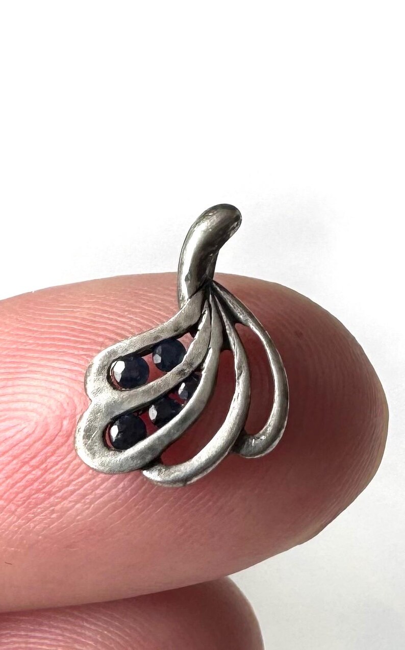 Op de afbeelding: Een zilveren hanger met een delicaat, abstract ontwerp met meerdere gebogen lijnen en bezet met kleine, donkerblauwe edelstenen.