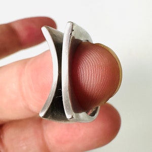 May include: A silver ring with a unique, geometric design. The ring is made of two pieces of metal that intersect at a sharp angle, creating a modern and edgy look.