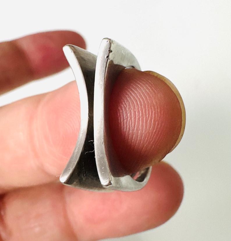 May include: A silver ring with a unique, geometric design. The ring is made of two pieces of metal that intersect at a sharp angle, creating a modern and edgy look.