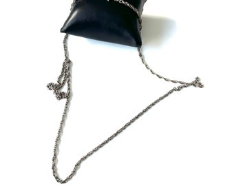 May include: A silver chain necklace on a black velvet cushion. The chain is a twisted rope style.