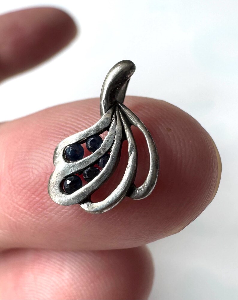 Op de afbeelding: Een zilveren hanger met een bladontwerp en blauwe edelstenen. De hanger is gemaakt van sterling zilver en heeft een delicaat, ingewikkeld ontwerp.