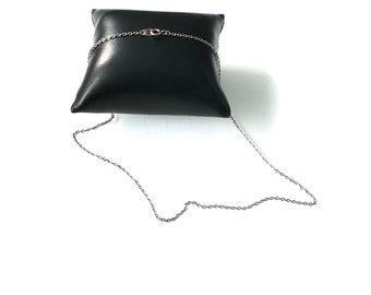 May include: A silver chain necklace displayed on a black velvet pillow. The chain is made of small, linked ovals.