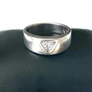 May include: A silver band ring with a triangular-shaped clear gemstone in the centre.