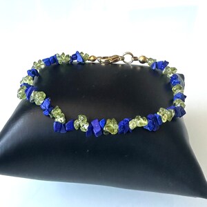 May include: A bracelet made of small, irregular pieces of green and blue gemstones. The bracelet is on a black pillow.