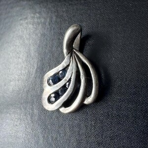 Op de afbeelding: Een zilveren hanger met een gestileerd ontwerp met meerdere gebogen lijnen en kleine blauwe edelstenen.
