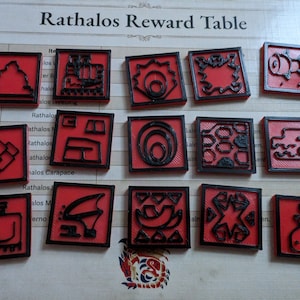 Könnte beinhalten: Eine Sammlung roter quadratischer Spielmarken mit schwarzen Umrissen, die verschiedene abstrakte Designs zeigen. Die Spielmarken sind auf einem bedruckten Spielbrett mit der Aufschrift "Rathalos Reward Table" angeordnet.