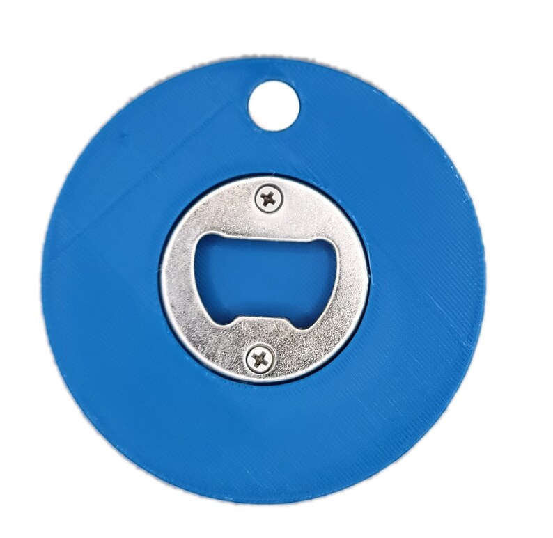Puede incluir: Un abridor de botellas redondo azul con un abridor de metal plateado en el centro. El abridor tiene un peque&ntilde;o agujero en la parte superior para sujetar un llavero.