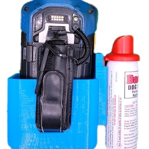 May include: A blue and black electronic device with a black leather case is held in a bright blue holder. A can of dog repellent with a red top is next to the device. The can has the words "Bad Dog" on it.